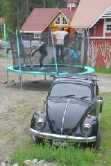 Lahjaksi saatu trampoliini on ollut ahkerassa käytössä. Edessä VW vm. 1969 ja takana liiteri sekä raitisilmatalli. Graniittikivistä on tehty taideteos ratastuskentän kulmaan.